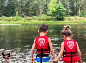 Two small children holding hands in the river, wearing LFD Life Jackets.